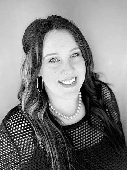 A woman with long hair wearing pearls and smiling.